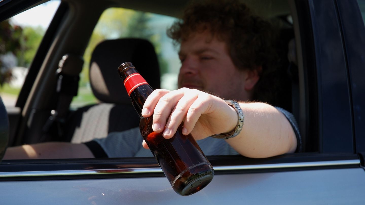 Man Holding A Beer Bottle While Seated In A Car 